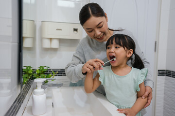 mother teaching girl child to brushing teeth in bathroom