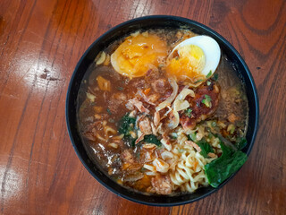 ramen noodles served in a bowl rich savory broth with jammy boiled egg, green vegetables, fried shallots, and onion slices. Top view, flat lay, restaurant dish.