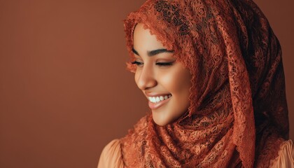 Young woman wearing an ornate terracotta lace headscarf beams a warm smile against a warm solid background