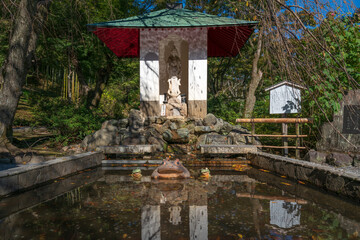 Statue of the Goddess of Mercy Kannon and the fountain with sculptures of frogs on the territory of the Tenryu-ji Buddhist Temple on a sunny autumn day, Kyoto, Ukyo Ward, Japan