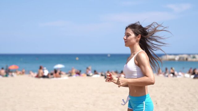 A woman runs on a beach with a crowd of people watching her. The beach is crowded with people, some of whom are sunbathing. The woman is wearing a bikini and is running on the sand