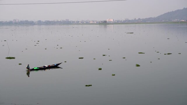 Lone fisher in a country boat at Deepor Beel in Guwahati Assam with the city in the background
