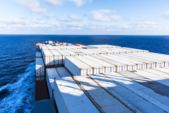 View from the bridge towards the bow of a container vessel with white reefer containers on deck, sailing through calm ocean waters.