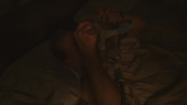 senior citizen puts on CPAP harness at night on his head for nighttime breathing treatment therapy