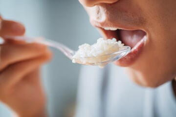 A hand holding a plastic spoon to eat rice; micro plastic contamination in food concept.