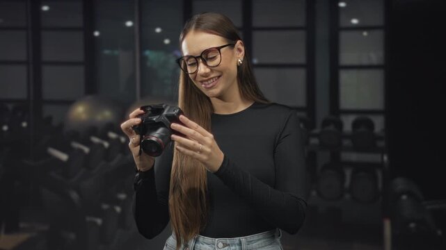 Woman photographer examines dslr camera in hands, smiling while checking settings with camera strap visible in studio; joy.