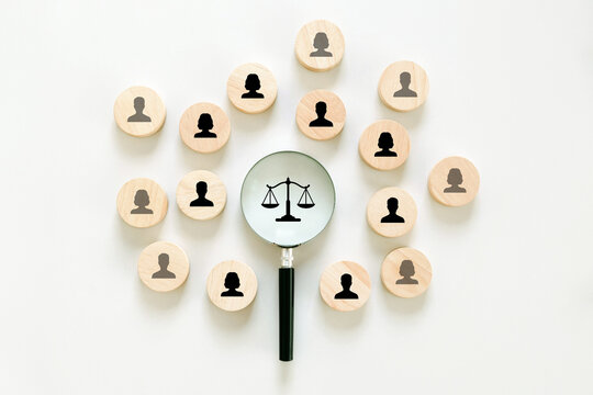 Human rights and equality law concept with wooden human icons surrounding a magnifying glass showing a justice scale. fairness, legal protection, social justice, diversity, and equal rights in society