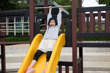 Excited Asian girl sliding quickly down a bright yellow playground slide, shouting with joy and adrenaline © Kwangmoozaa