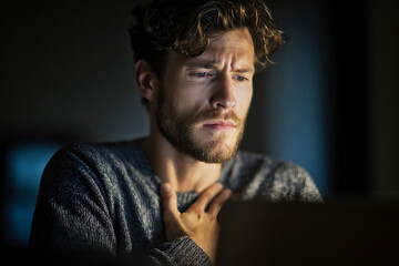 Obraz premium Thoughtful man with hand on chest showing concern while looking at a screen in a dark indoor space