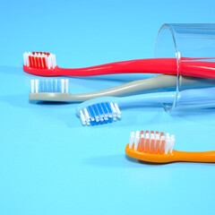 Assortment of brightly colored plastic manual toothbrushes arranged in clear glass on a blue background for oral hygiene product comparison, Selective focused, closeup view 