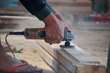 A carpenter is smoothing wood with a grinder. Workers in the home improvement industry are focused on making wooden cabinets and preparing boards for interior projects.