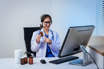 An Asian female doctor wearing a headset presents medicine bottles during an online consultation, demonstrating telemedicine services, digital healthcare communication,remote diagnosis, professional