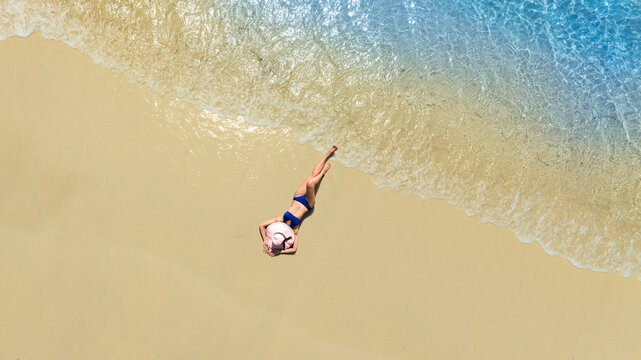 Aerial view of beautiful young woman in black swimsuit lying on sandy beach near blue sea with waves at sunset Summer vacation at Andaman Island	
