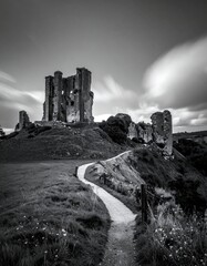 Black & white photo of a weathered stone structure on a hilltop, long-exposure clouds, winding path in foreground
