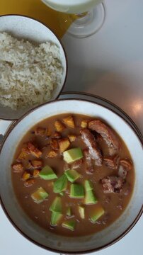 Vertical video showcasing a close-up of traditional Colombian cazuela de frijoles with avocado and pork, ideal for mobile and social media use. Medellin Food.