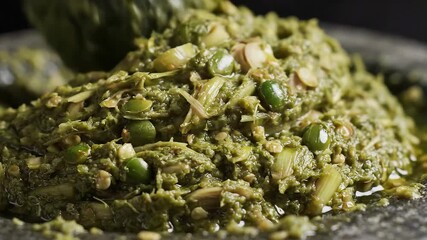 Closeup view of vibrant green chili paste being freshly ground in a traditional mortar and pestle showcasing the rich texture and aromatic blend of spices and herbs for authentic culinary preparation.