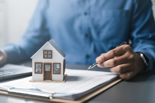 Mortgage and real estate finance concept showing house model on documents with professional signing, representing home loan calculation, property investment, interest rates, and financial planning.