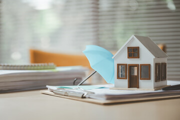 Mini house protected by umbrella on documents representing home insurance, property coverage, risk...