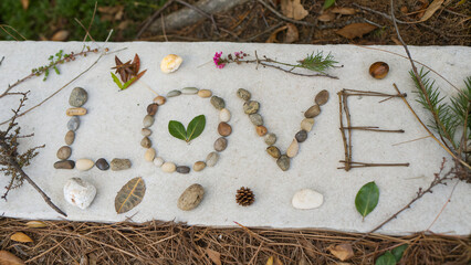 Creating a natural art piece using sticks, stones and leaves to spell out love on a white background 