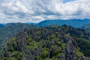 Fototapeta premium Sharp limestone spires rise above dense green forest under a dramatic sky in the rural countryside of Laos. The rugged formations and vibrant vegetation create a striking natural landscape typical of