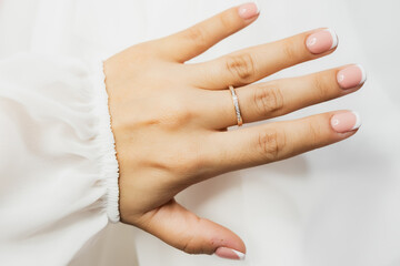 A woman's hand with a ring on it. The ring is gold and has diamonds. The woman is wearing a white...