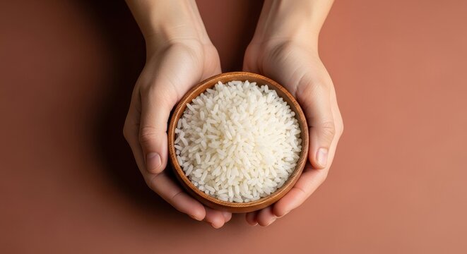 Hands gently hold a wooden bowl filled with white uncooked rice grains, showcasing nourishment and staple food preparation