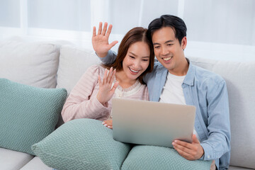 Happy asian couple video call on laptop together in living room at home, man and woman talking online cyberspace at home, technology connection and social media interaction, relationship and bonding.