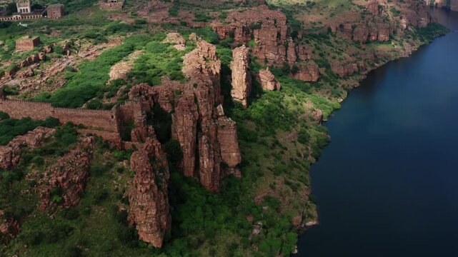 Drone glides forward over Gandikota Fort's ancient red stone ruins perched on canyon edge, revealing Pennar River reservoir below amid sparse green vegetation.