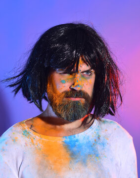 Funny crazy man with beard and wig in holi color on face. Expressive crazy male portrait with paint on face. Crazy male emotions and fun. Crazy funny bearded man in wig.
