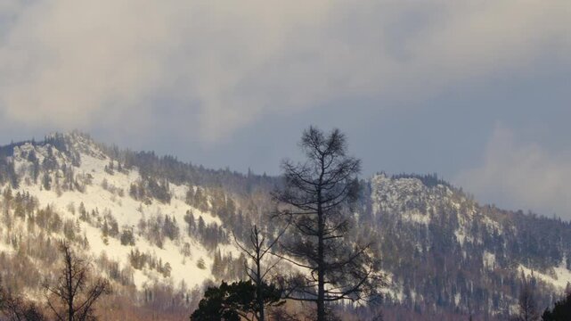 footage capturing the majestic, snow-dusted peaks of the Southern Ural Mountains in Russia. The scene features sparse forestation with a dramatic cloudy sky, highlighting the rugged beauty of the remo