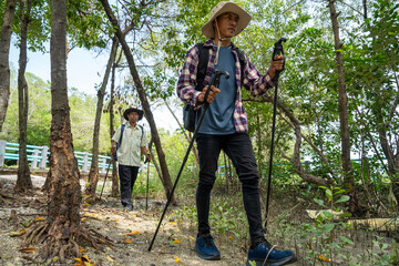 Two male friends with backpacks on vacation hiking through countryside together. Man tourists with backpacks and hiking equipment are walking in the forest. People on mountain hike with trekking poles