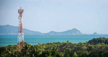 Obraz premium Mobile communication tower above tropical forest with turquoise sea, distant island mountains, wide blue sky