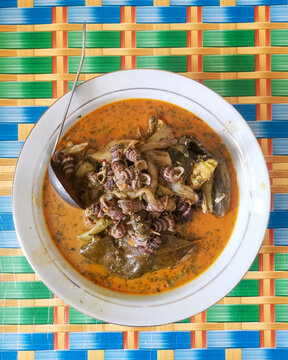 Top view of traditional spicy river snail  or Tutut or Tengkuyung and Taro curry in white bowl on colorful woven mat background, authentic Indonesian village food concept.