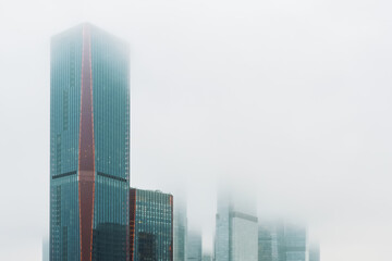 Fog covers modern buildings in a city skyline during morning hours.