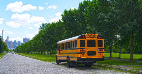 Yellow school bus parked on a city road. School transportation vehicle. Classic yellow school bus in a summer city. School bus waiting along a quiet road in an urban park.