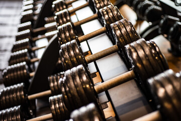 Fototapeta premium Dumbbells on a gym rack. Training sport power equipment. Dumbbells arranged in rows for gym workout. Dumbbells made of heavy metal for muscle building. Dumbbells in a modern gym.