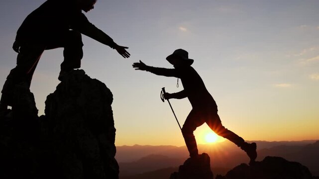 Silhouette of  Two climbers assist one another while scaling a rocky mountain under a breathtaking sunset. business success, leadership, achievement and people concept.