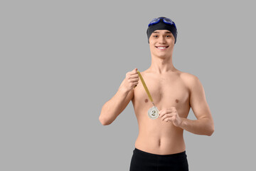 Young male swimmer with second place medal on light background
