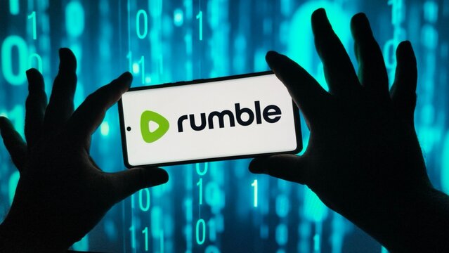 Hands hold smartphone displaying rumble logo against binary code