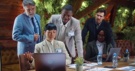 Multiracial business team focused on laptop analysis during meeting as Japanese businesswoman leads discussion and presents data in modern eco office, collaboration and strategic planning concept. - Powered by Adobe