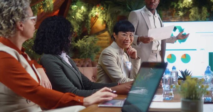 Smiling Japanese businesswoman looking at camera while seated at conference table during business meeting and presentation in a modern eco office.