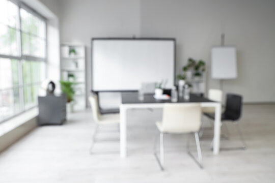 Blurred view of light office with meeting table and projector screen - Powered by Adobe