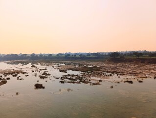 Naklejka premium Serene River Landscape at Sunset with Rocky Bed and Distant Treeline