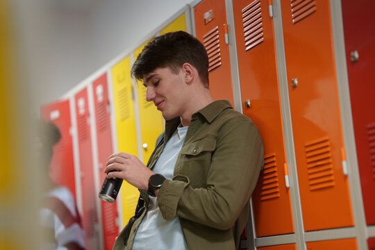 Teen student drinking an energy drink in school hallway.