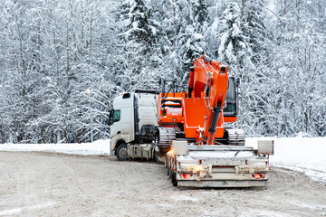 Rear view tow truck with excavator parked in winter on snowy trees background. Heavy equipment...
