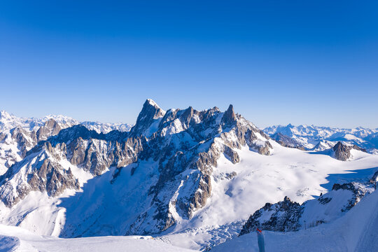 Jagged snow-covered peaks of the Grandes Jorasses rise above the expansive Glacier du Geant under a vivid blue sky, creating a dramatic alpine landscape in the Mont Blanc massif.