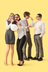 Obraz premium Business colleagues in funny disguise with balloon on yellow background. April Fools' Day celebration