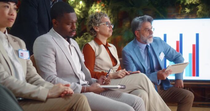 Multiracial business team listening to a speaker during a seminar or meeting, taking notes in a modern office, as a Black man raises his hand to ask a question, corporate training and development.