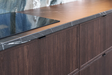 Contemporary kitchen interior with dark wooden cabinets and marble countertops.