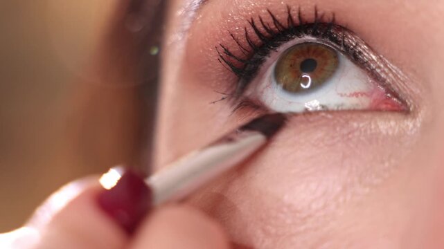 Professional makeup artist applying blush, lipstick and fixing spray to smiling woman in modern beauty salon. Close up shots of eyeshadow palette, brush on eyelids, warm golden colors and wooden inter